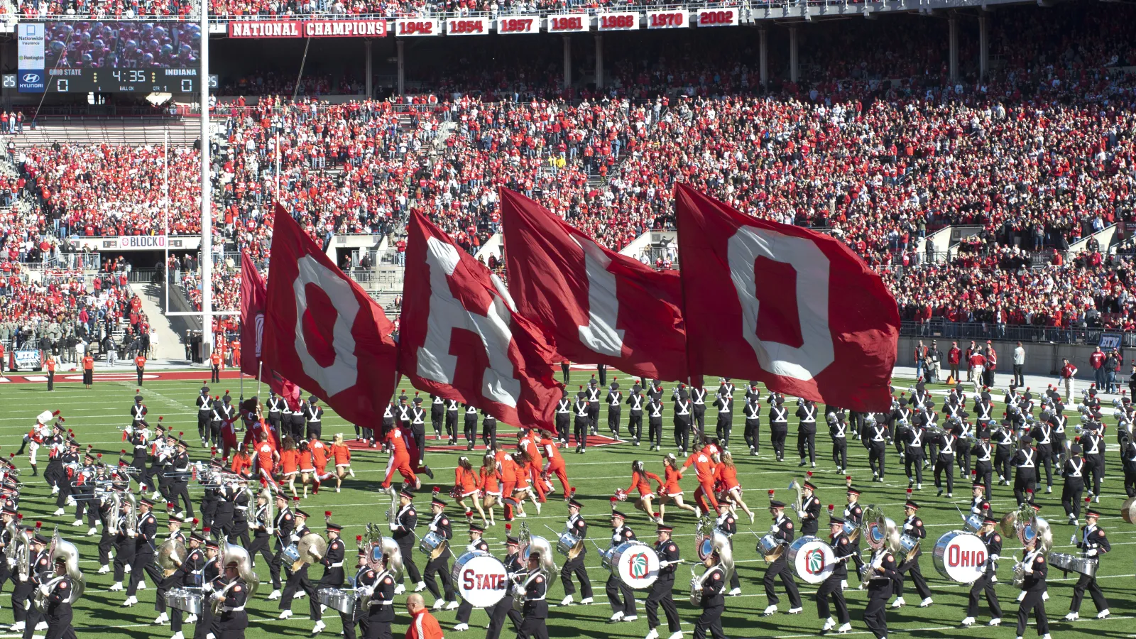 Picture of cheerleaders running with OHIO flags at an OSU football game